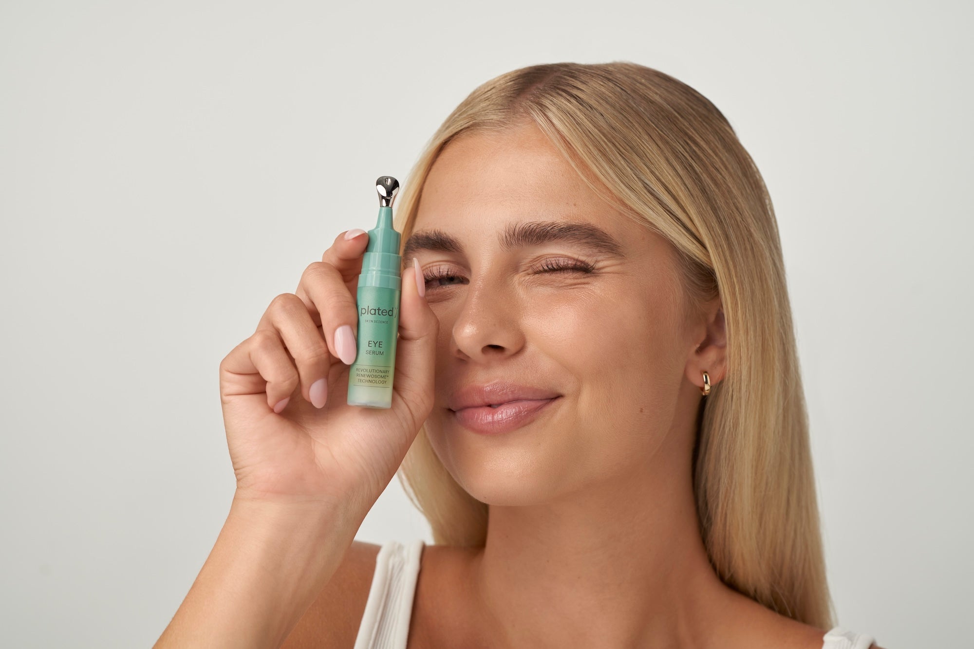 Model holding a green bottle of ( plated ) EYE Serum near her face and winking