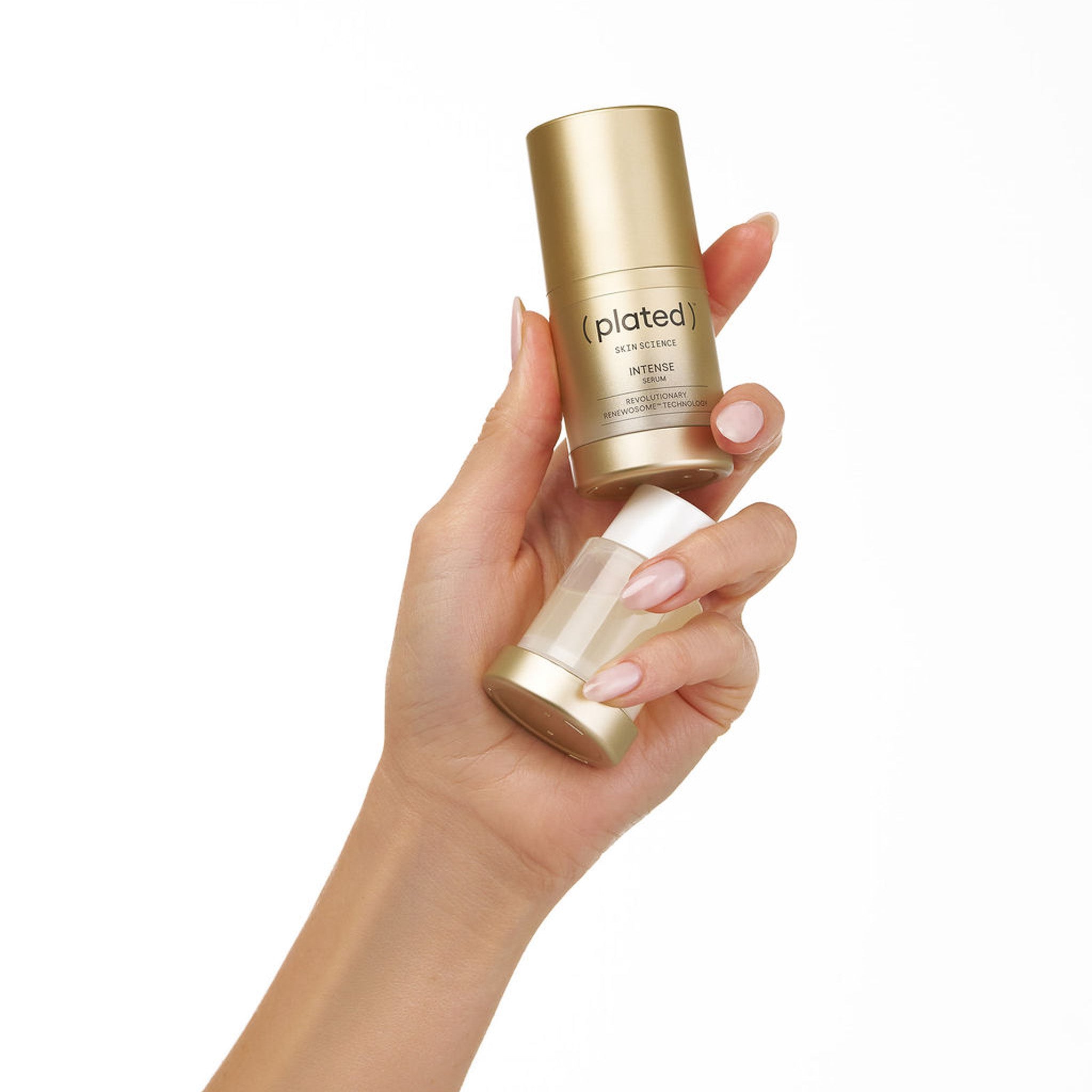 Hand holding a gold bottle of INTENSE Serum and an INTENSE Serum Refill cartridge with ( plated ) branding on a white background