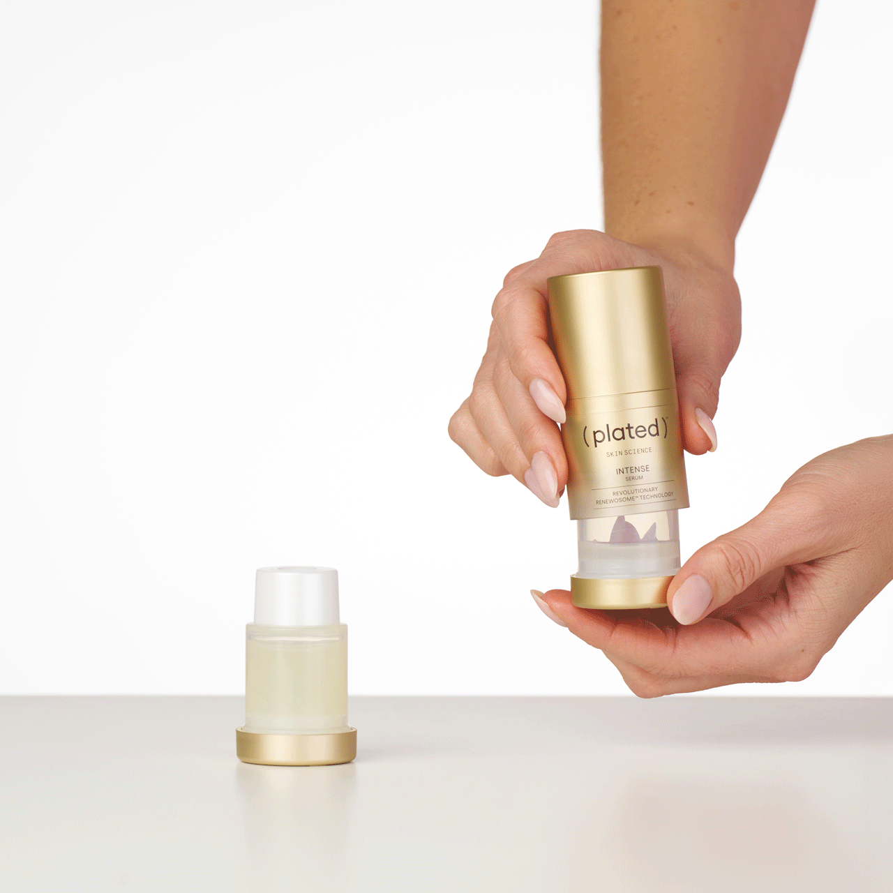 Hands holding a ( plated ) Skin Science INTENSE Serum bottle and refill cartridge on a white background - Step 2 of the Refill Sequence