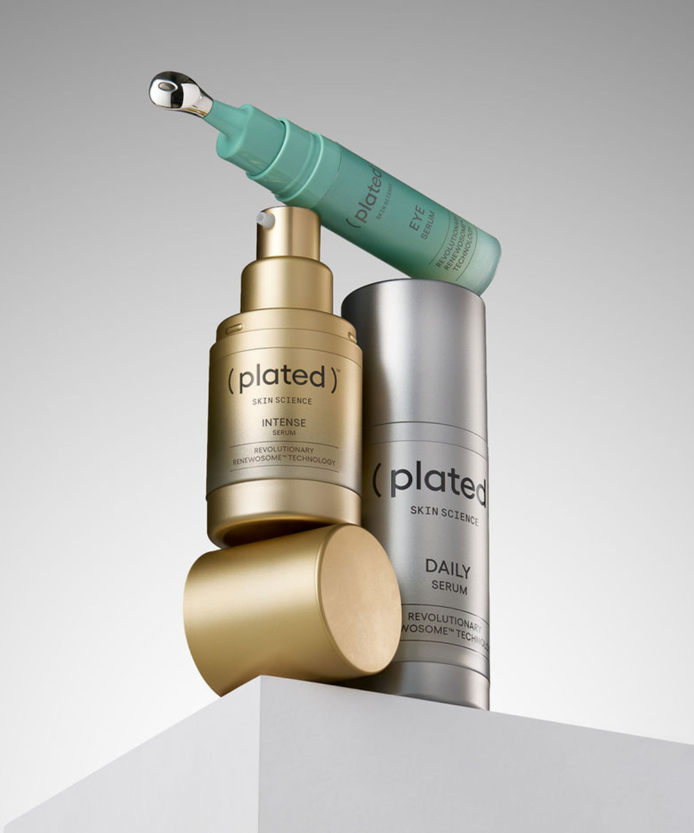 ( plated ) skincare products, including a gold bottle, silver tube, and green applicator, on a grey background.