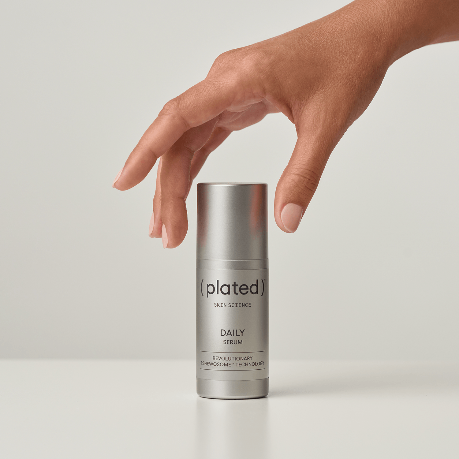 Hand reaching towards a silver ( plated ) DAILY Serum skincare bottle a light background