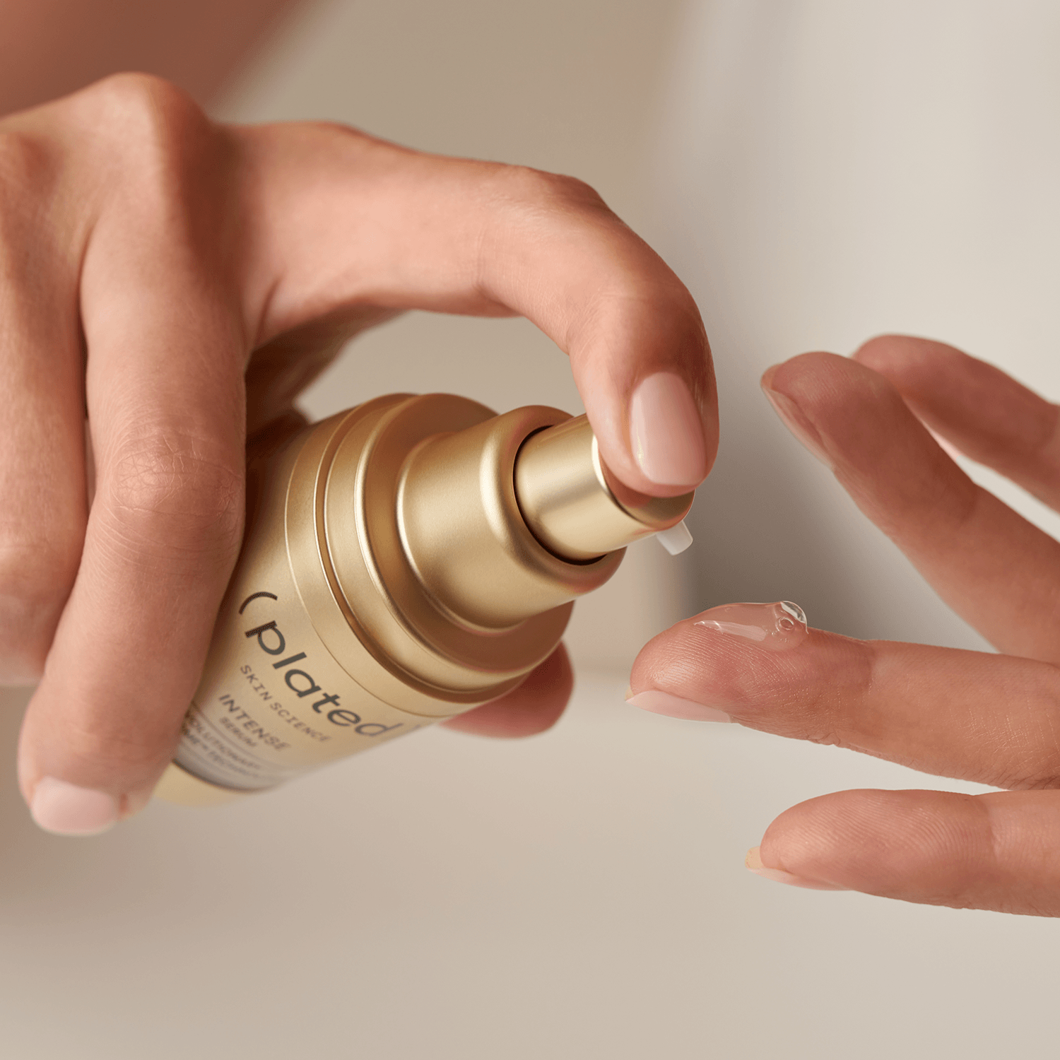 Hand holding a gold ( plated ) INTESE Serum bottle, applying product to another hand.