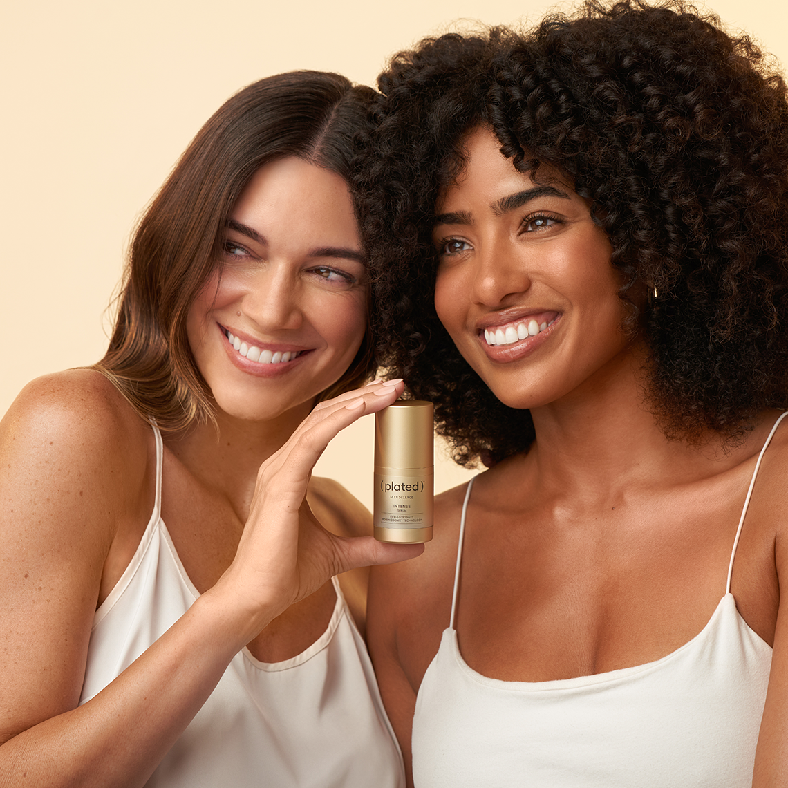 Two women holding the INTENSE Serum 15 mL full-size bottle against a beige background