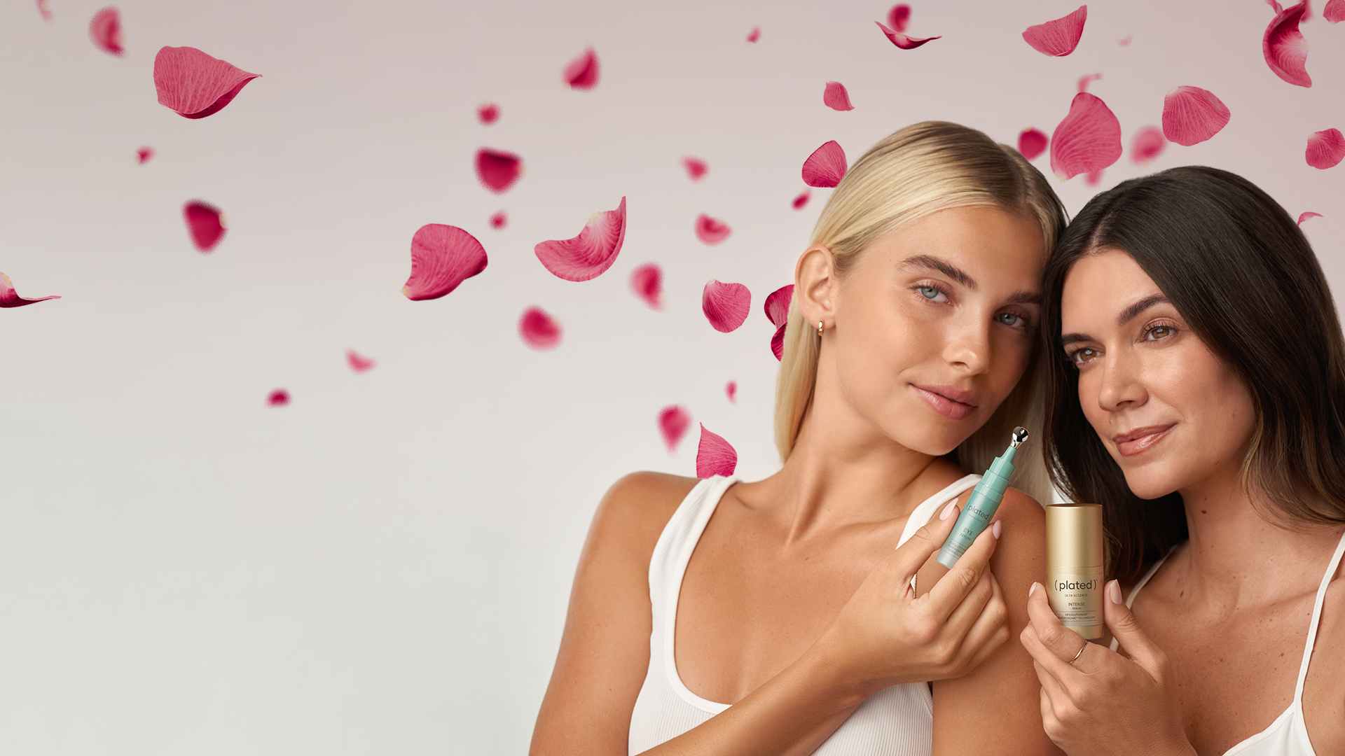 Models holding INTENSE & EYE Serum skincare products with pink flower petals on a grey background